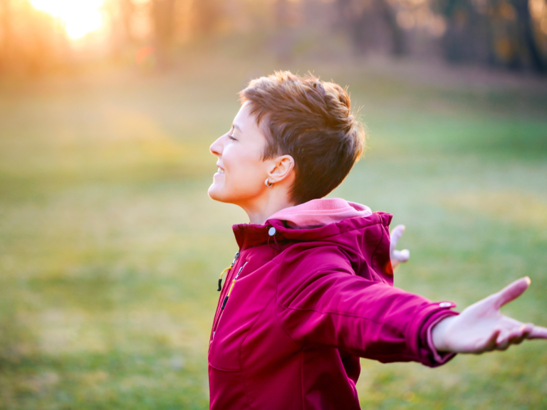 Woman wearing a red jacket stands with her arms wide enjoying the sun