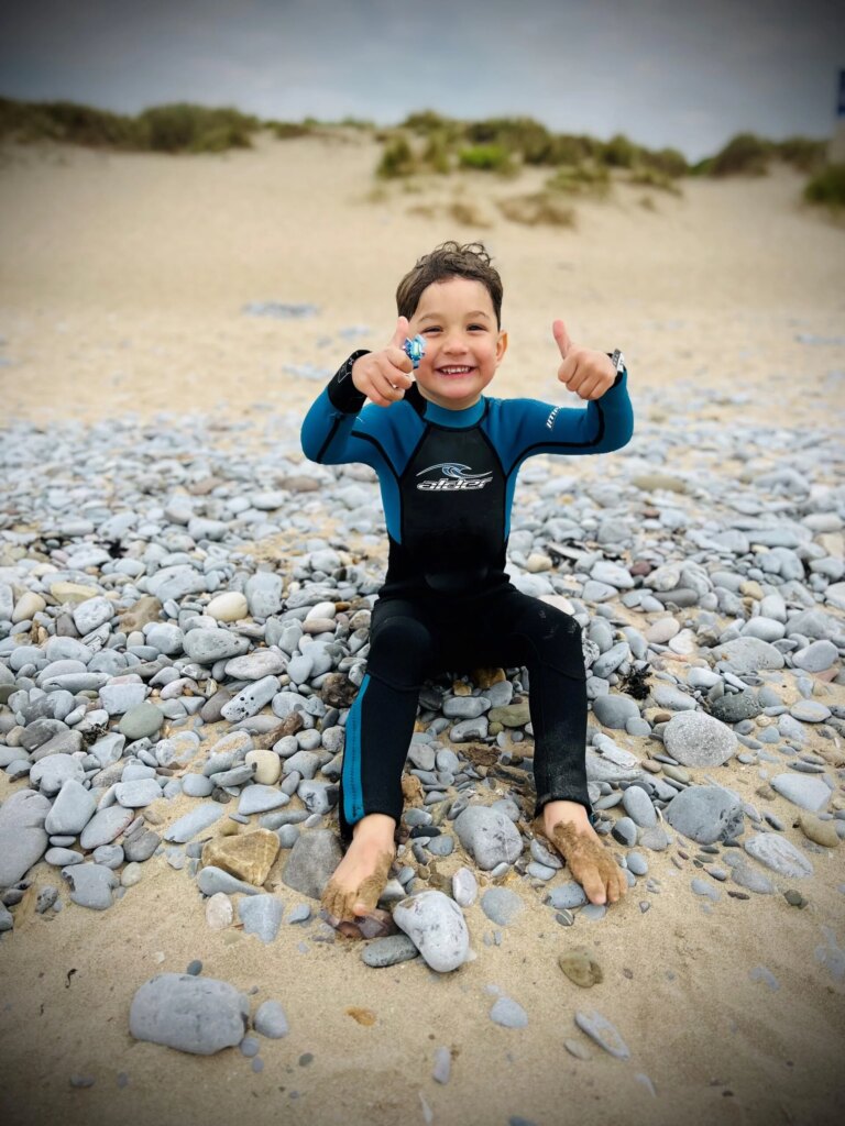 young boy smiling at the camera in a swimming suit on the beach