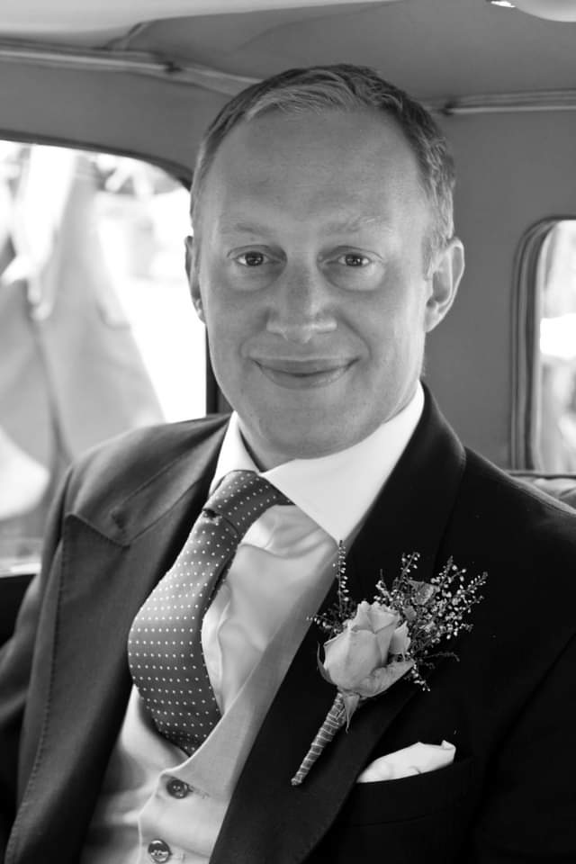 black and white photo of middle aged male dressed smartly and smiling at the camera